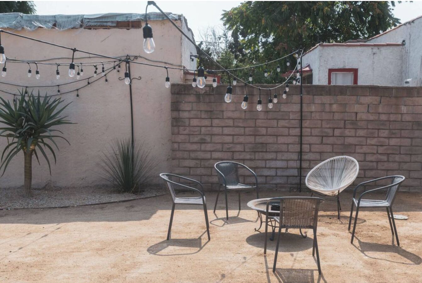 A patio with four metal chairs and a small table, a string of hanging lights, and a brick wall.