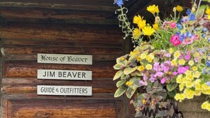 Eine Holzhütte mit einem Schild, auf dem steht: 'House of Beaver, Jim Beaver, Guide & Outfitters'.