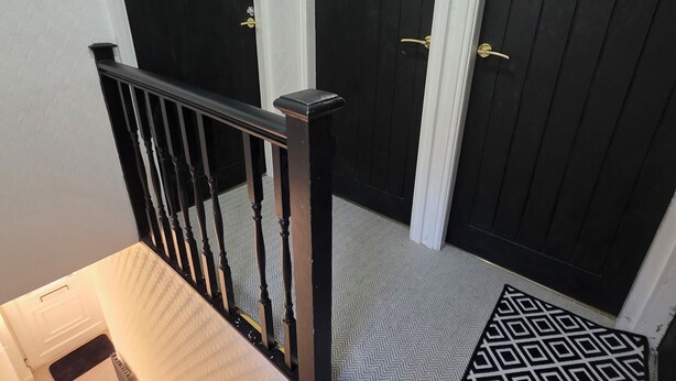 A staircase with a black railing leading to a landing with three dark wooden doors, each with a brass handle.