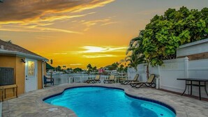 A swimming pool with lounge chairs, a patio area, and a view of the sunset.
