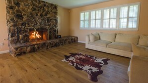 Un salon avec une cheminée en pierre, un canapé beige, un plancher en bois et un tapis en peau de vache.