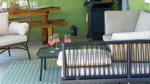 Un salon accueillant avec un fauteuil en osier, un canapé et une table sur laquelle sont posés trois verres remplis d’une boisson rose.