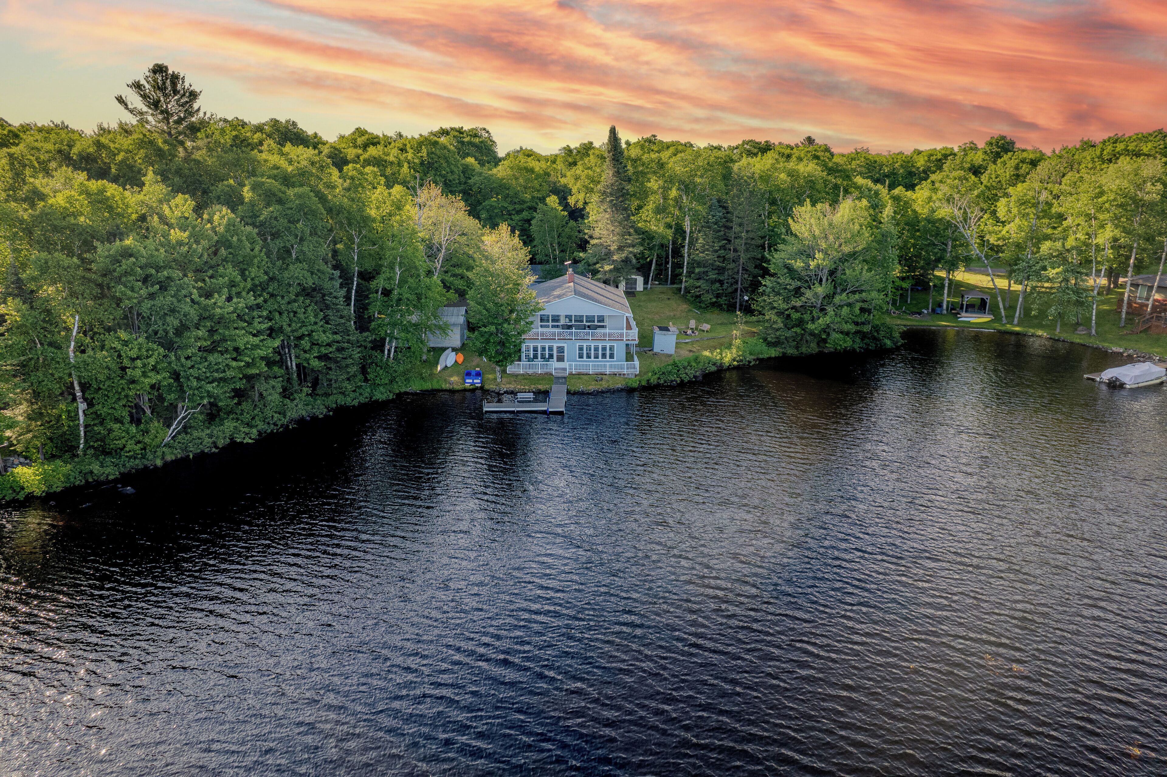 Una casa frente al lago con un muelle, rodeada de un bosque frondoso.
