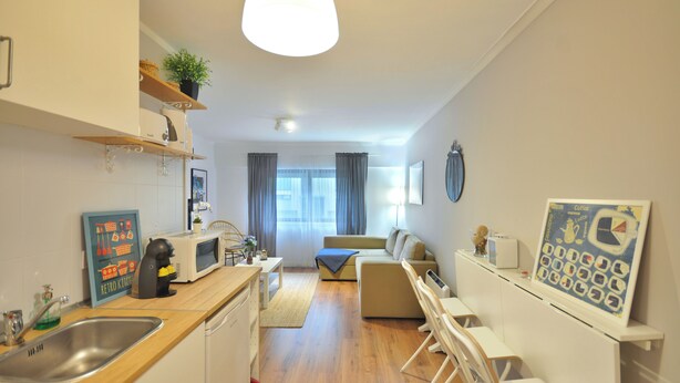 Una cocina moderna con encimera de madera, un lavamanos y un microondas. En la sala de estar hay un sof á y una mesa de comedor.