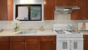 Una cocina con armarios de madera, una encimera blanca, un fregadero, una estufa y una ventana con vistas a árboles.
