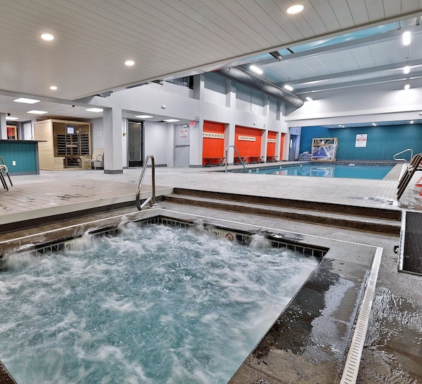 A swimming pool area with a hot tub, steps leading to the pool, and a changing room in the background.