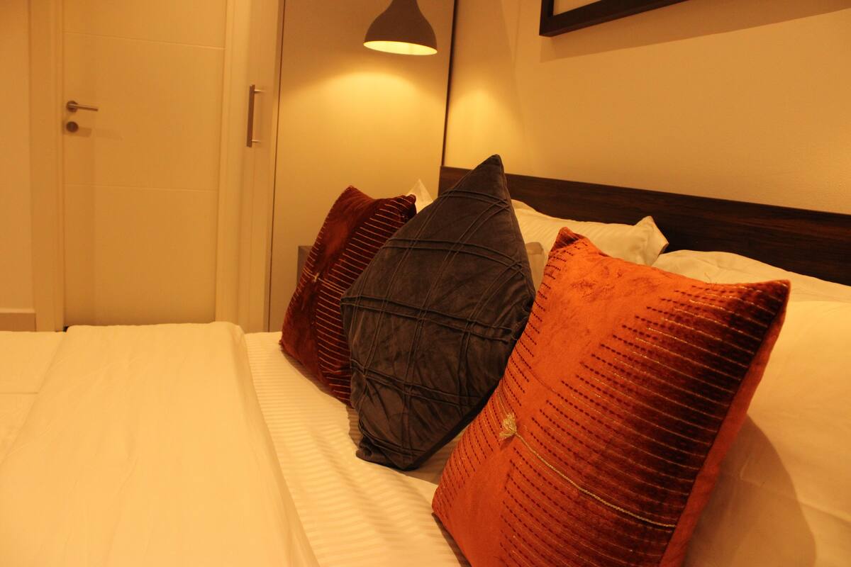 A neatly made bed with multiple pillows and a bedside lamp.
