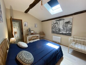 Un dormitorio con una cama, una cuna, un tocador, un espejo y un tragaluz en el techo.