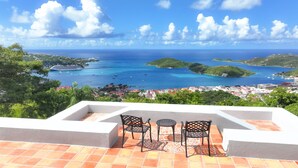 A terrace with two chairs and a table, overlooking a coastal town and the sea.