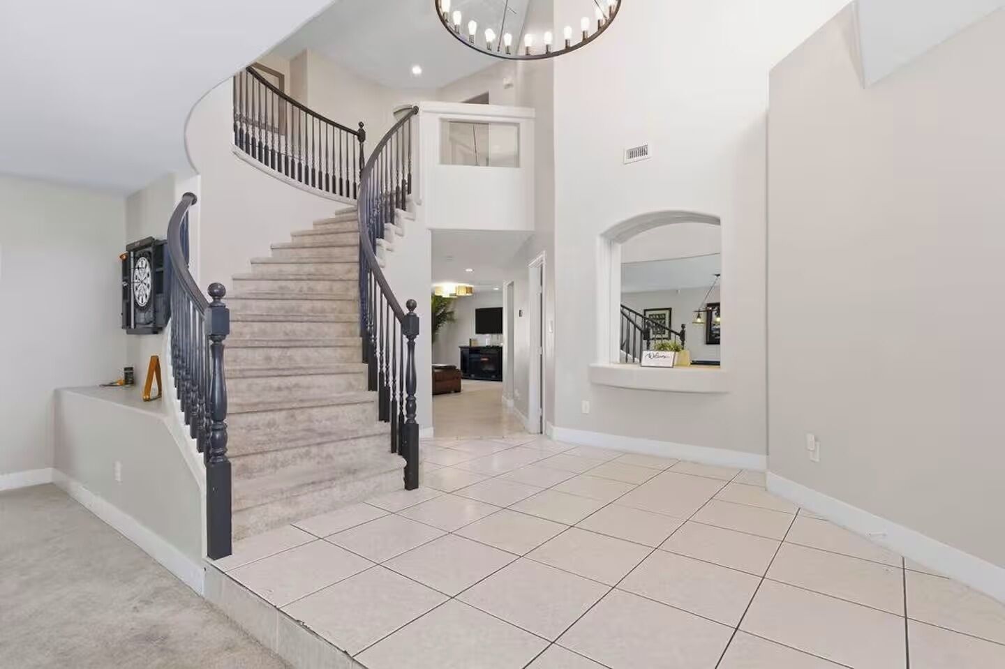 A spacious interior with a central staircase, a kitchen area in the background, and a large open space with tiled flooring.
