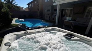 A hot tub with a pool in the background, a patio area, and a building with windows and shutters. - The Vegas Villa, Entire Home in Las Vegas, Nevada (Las Vegas)