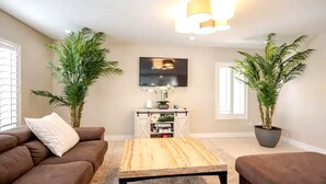 A living room with a brown sofa, a wooden coffee table, and two potted plants. - The Vegas Villa, Entire Home in Las Vegas, Nevada (Las Vegas)