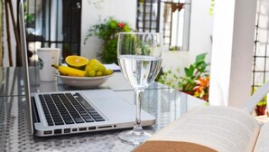 Een laptop op een glazen tafel, met een glas water, een schaal fruit en een open boek.
