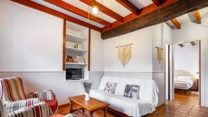 Een woonkamer met een bank, gestreepte fauteuils, een houten salontafel, een televisie en een wandplank met decoratieve objecten.