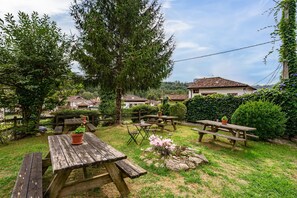 A rustic outdoor setting with wooden picnic tables, a large tree, and a well-maintained lawn.