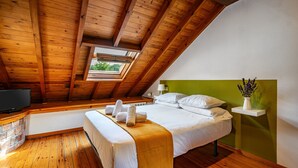 A bedroom with a wooden ceiling, a bed with white linens, a bench, a TV, and a small window.
