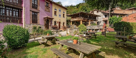 Un patio con mesas de picnic y plantas en macetas, rodeado de edificios de arquitectura tradicional.