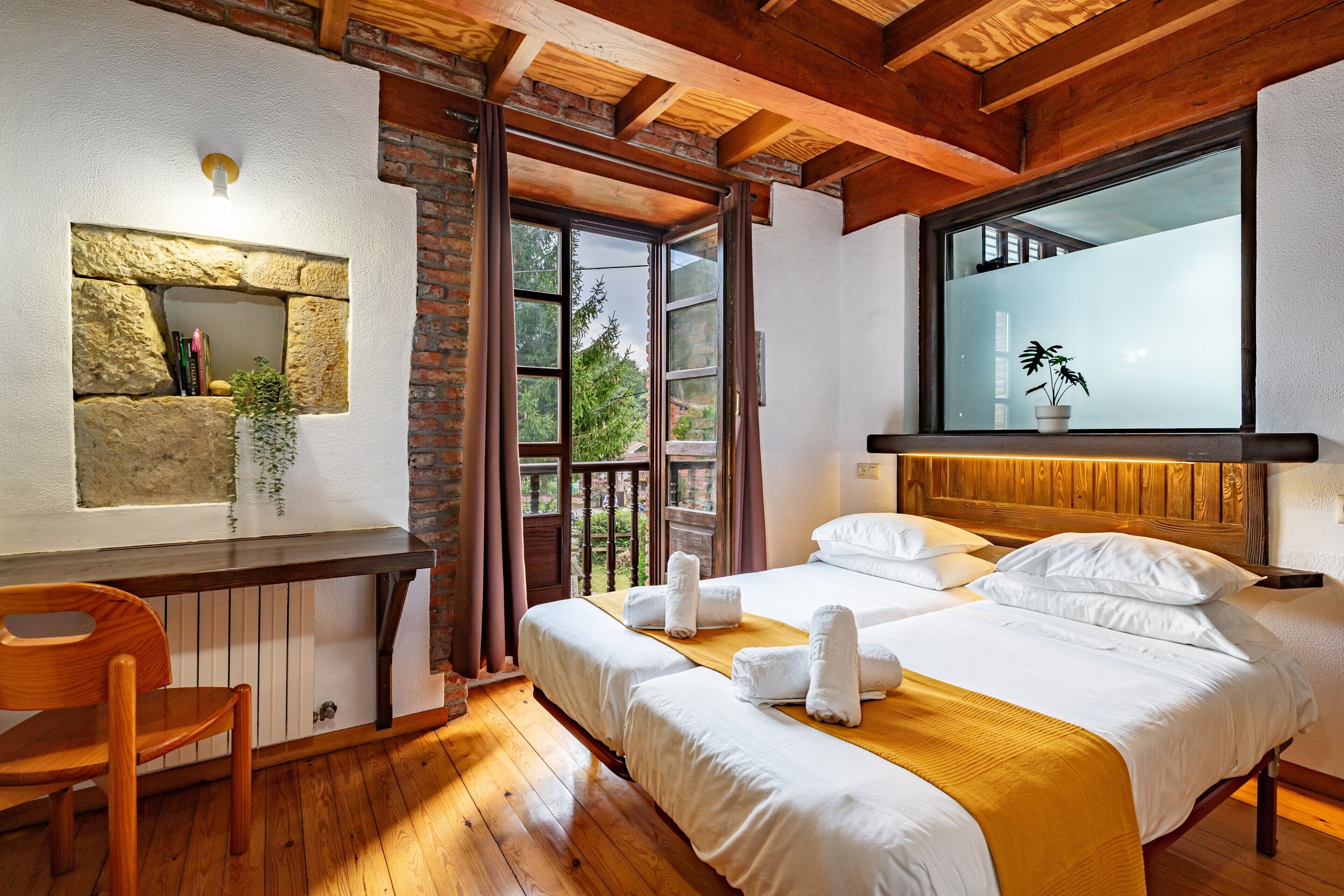 Una habitación con cama, escritorio, silla y ventana con planta.
