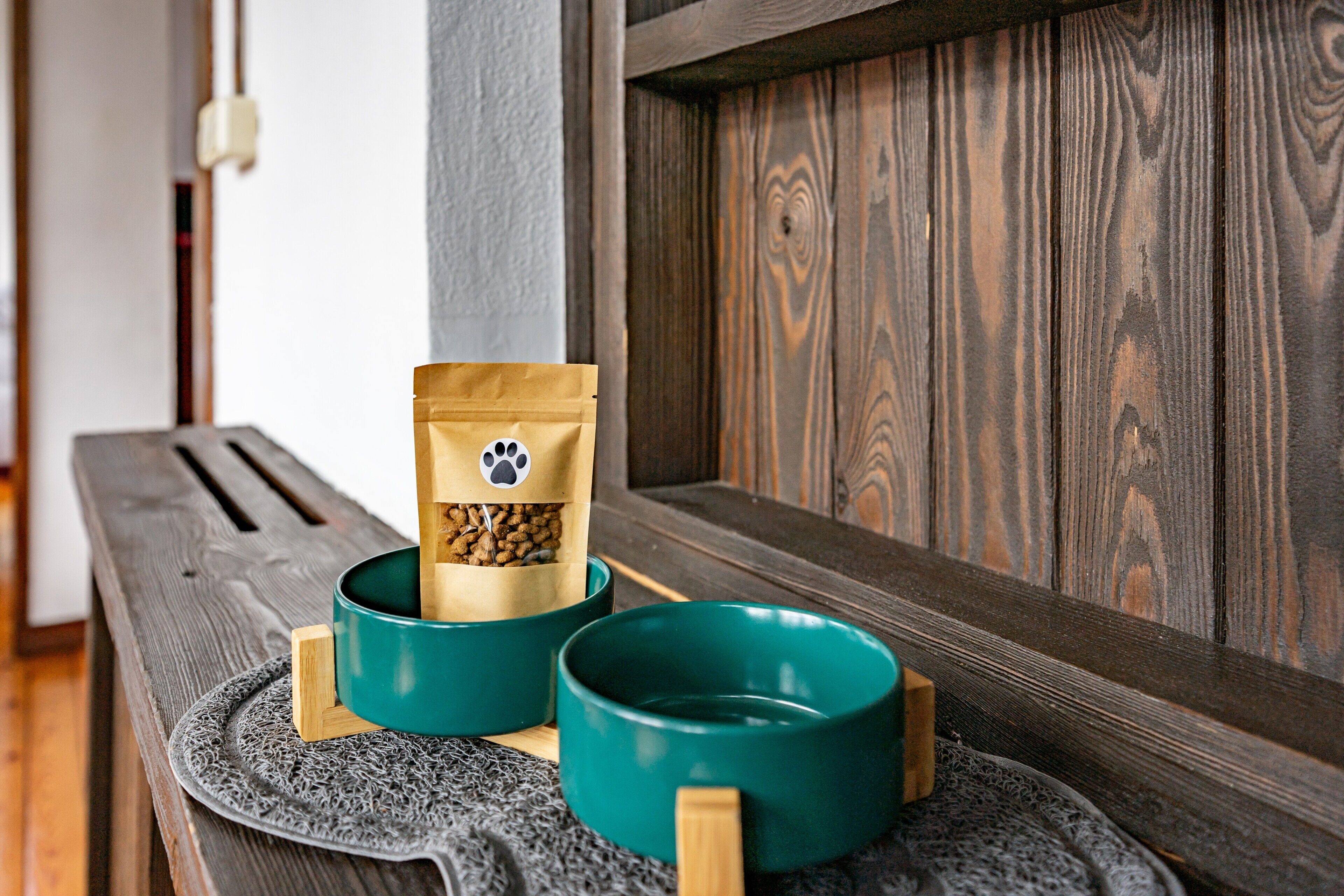 A wooden bench with two teal bowls and a brown bag with a paw print.