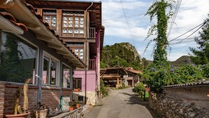 Une rue étroite bordée de bâtiments traditionnels, un mur de pierre et une montagne en arrière-plan.