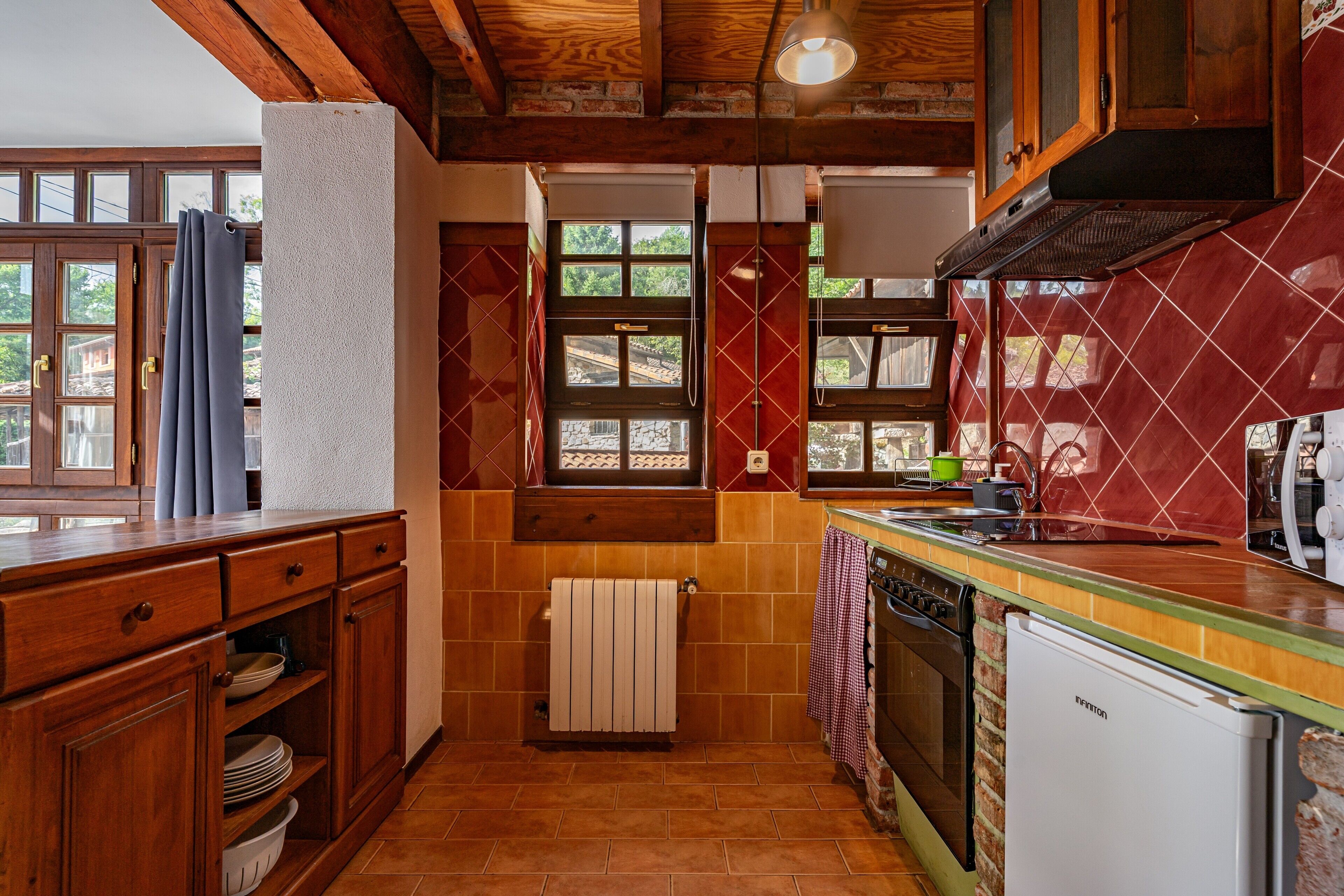 Una cocina con armarios de madera, salpicadero de azulejos, una ventana y horno empotrado.