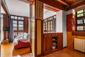 Een gezellige kamer met een rode bank, houten kasten en grote ramen.