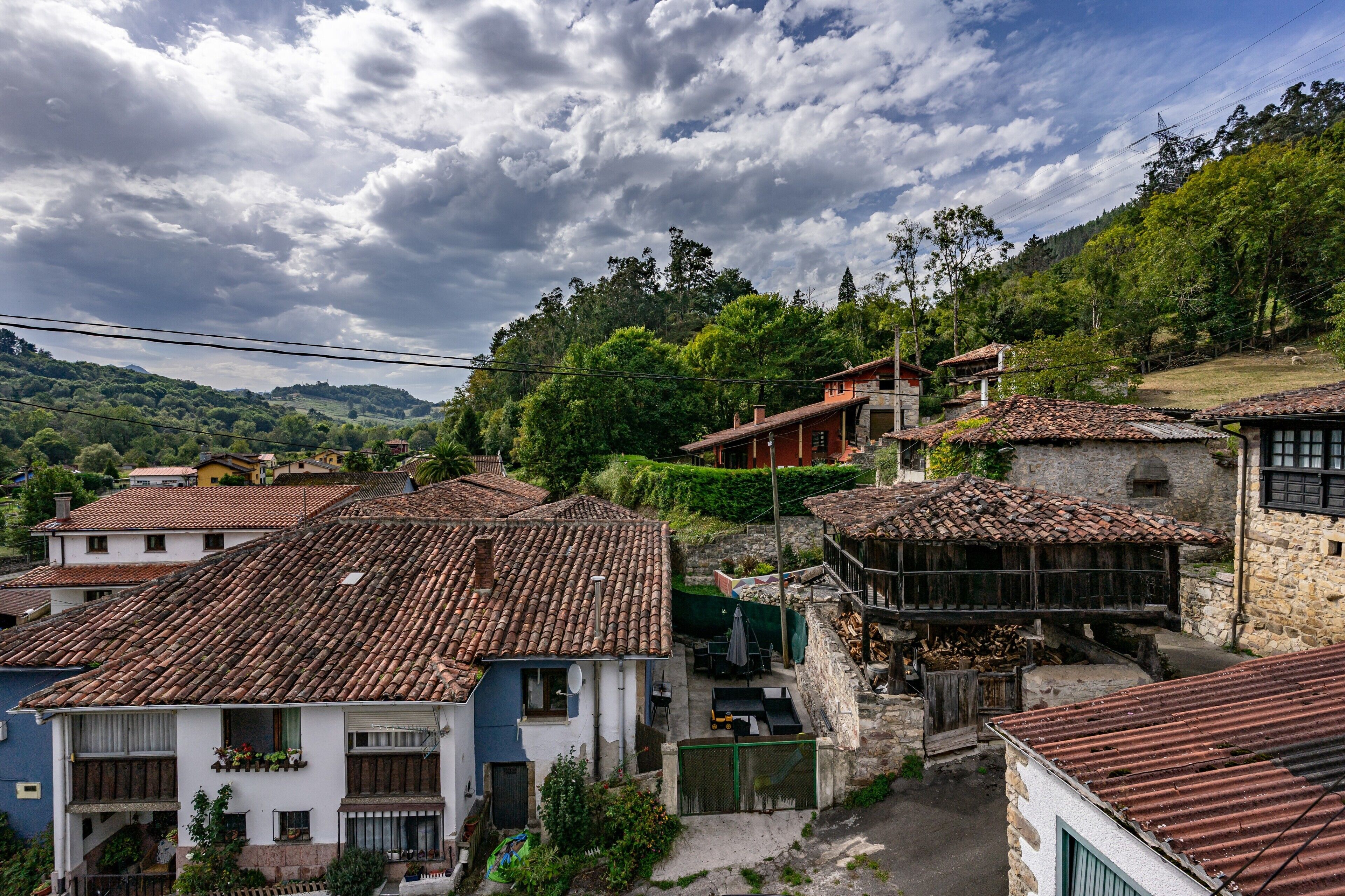 Un pueblo tradicional con edificios de tejados de terracota, un puente de piedra y abundante vegetación.