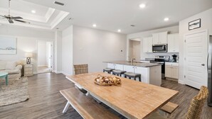 A modern kitchen with white cabinets, a large island, and a dining area with a wooden table and benches. - Falling Star Retreat is a 4BA/2BA coastal home, just 900 feet to the beach, pet friendly! (Port St. Joe)