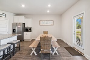 Eine Küche mit weißen Schränken, einem Edelstahlkühlschrank, einem Holzespeisetisch mit zwei Bänken und einem Schild mit der Aufschrift 'BEACH' an der Wand.