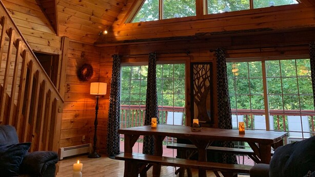 A cabin interior with a high ceiling, wooden beams, a dining table, and large windows overlooking a deck. - Bachelor Parties, direct access to Lehigh River to hike, bike, fish and swim. (White Haven)