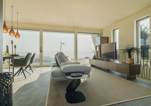 A modern living room with a sofa, a coffee table, a TV, and a balcony with a view.