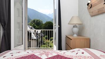 Une chambre à coucher avec un lit, une table de chevet, une lampe, une vue sur les montagnes et une porte donnant sur un balcon.