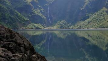 A serene lake with a waterfall, surrounded by lush green mountains and clear skies.