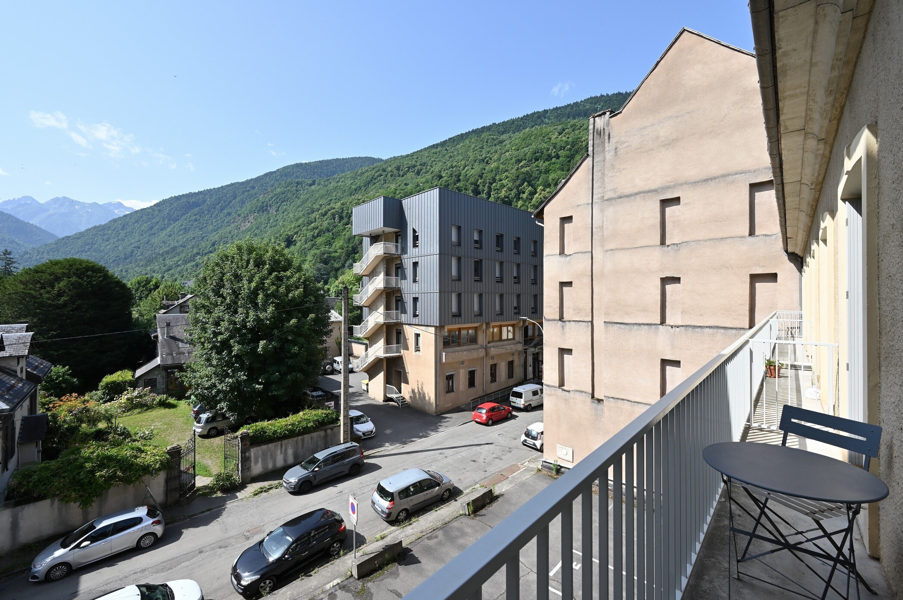 Un edificio residencial con balcón, vista a la calle y montañas al fondo.