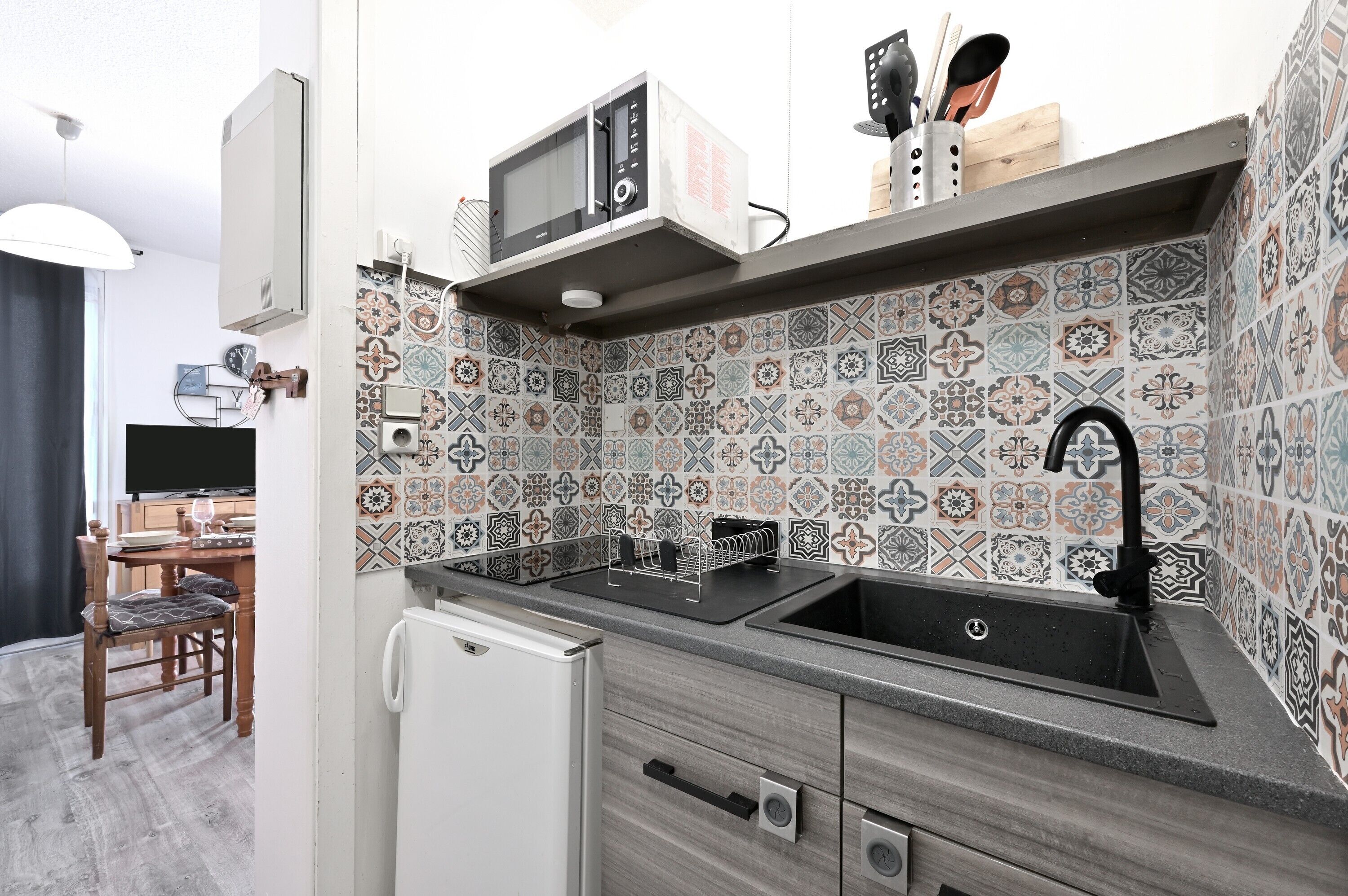 A kitchen with a microwave, sink, and patterned backsplash.