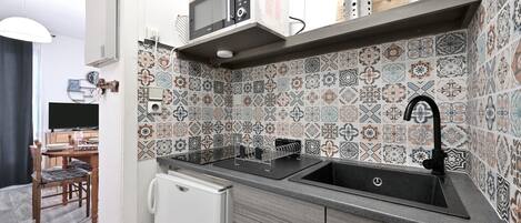 A kitchen with a microwave, sink, and patterned backsplash.