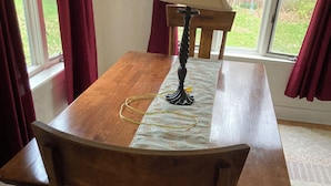 Una mesa de comedor de madera con un banco a cada lado, una lámpara de mesa y una ventana con cortinas.