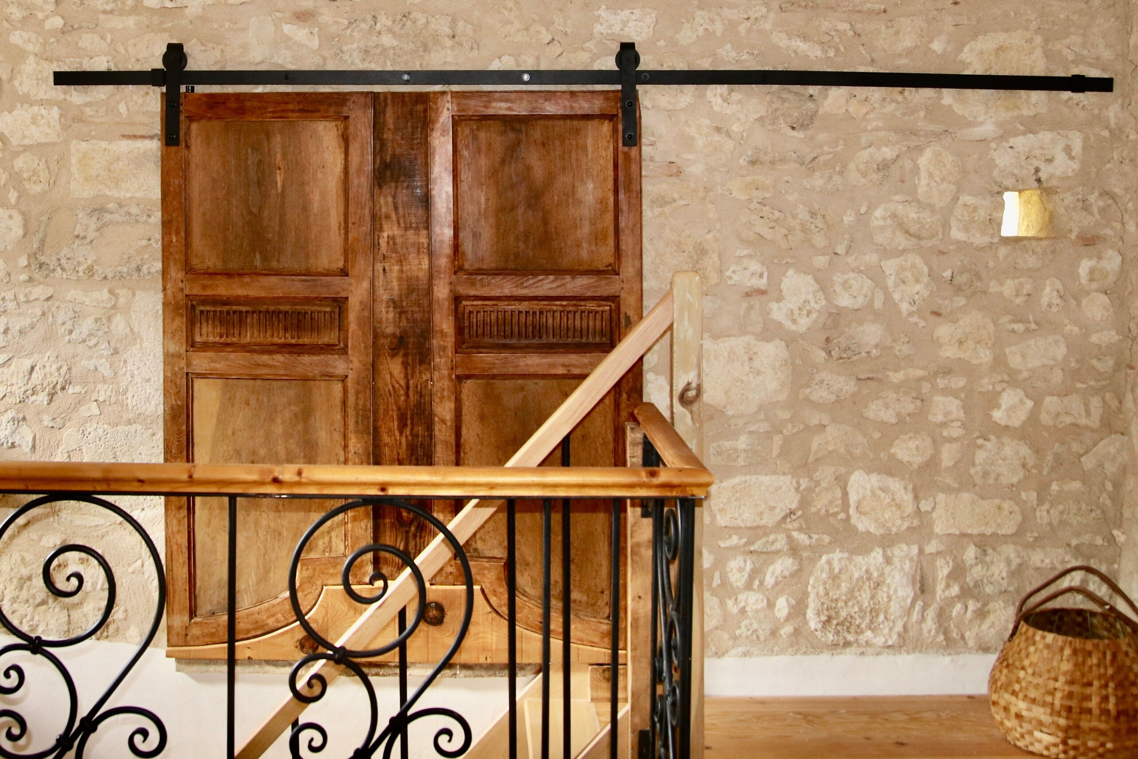 A wooden door with a black metal handle, a wooden staircase with a metal railing, and a stone wall.