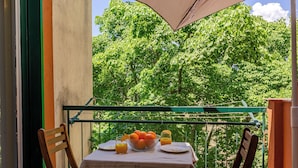Ein Balkon mit Tisch für zwei Personen, dekoriert mit einer Orangenschale, einem Glas Orangensaft und einem Teller Essen.