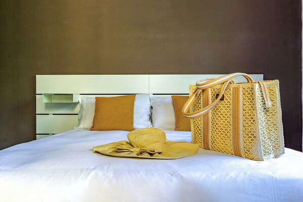A neatly made bed with a white comforter, two pillows, a yellow bag, and a woven bag on the bed.