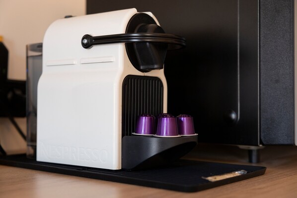 A Nespresso coffee machine with a black and white body, a black handle, and three purple capsules.