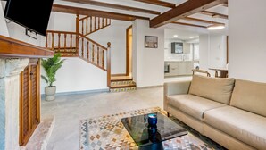 Una sala de estar con sofá, una mesa de centro, una escalera y una cocina al fondo.