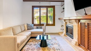 Una sala de estar con sofá, una mesa de centro, chimenea y ventana con vista a follaje.