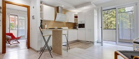 A modern kitchen with white cabinets, a central island, and a sliding glass door leading to a balcony.