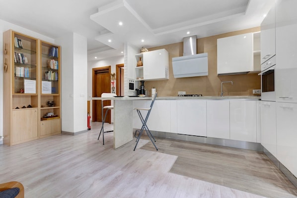 A modern kitchen with white cabinets, a central island, and a wooden bookshelf.