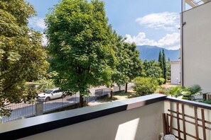 A balcony with a view of a street, trees, and mountains.
