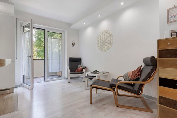 A modern room with a sliding glass door leading to a balcony, a wooden chair, a small white table, and a decorative wall piece.