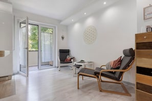 A modern room with a sliding glass door leading to a balcony, a wooden chair, a small white table, and a decorative wall piece.