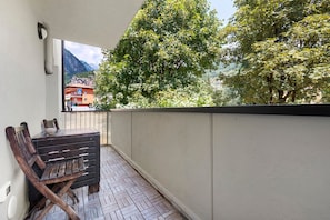 A balcony with a table and chairs, a view of trees and mountains, and a building in the background.