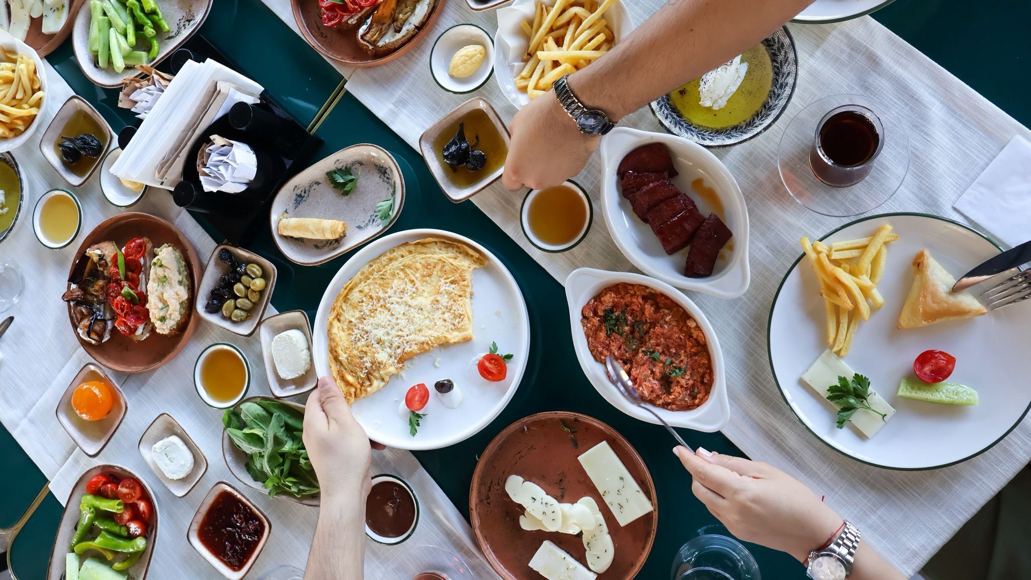 Una mesa con varios platos, incluyendo una tortilla grande, papas fritas y varios recipientes pequeños con salsas y aderezos.